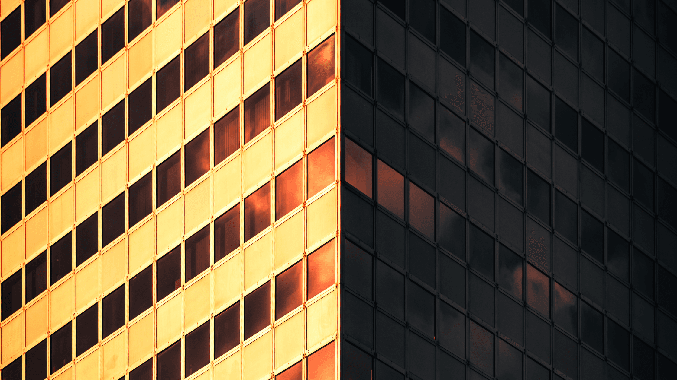 Golden and dark glass building façades meet at a sharp corner, reflecting sunlight and creating a striking contrast.