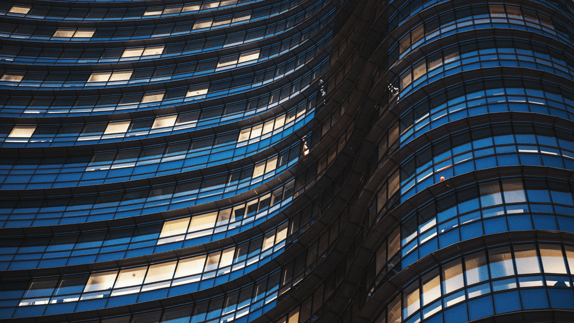 Curved glass facade of a modern building with illuminated windows at night.