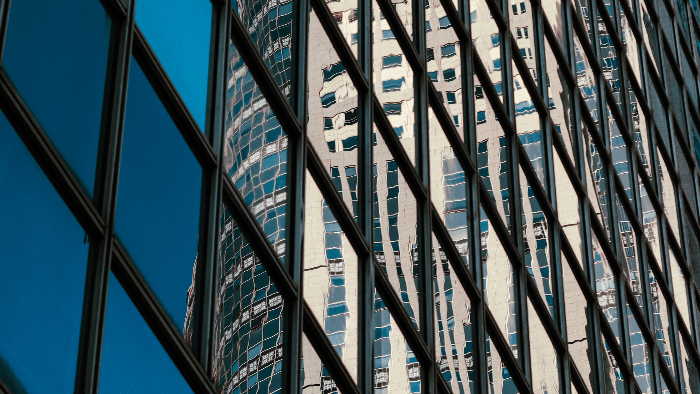 Skyscraper reflections on glass windows, creating a distorted and abstract pattern against a clear blue sky.