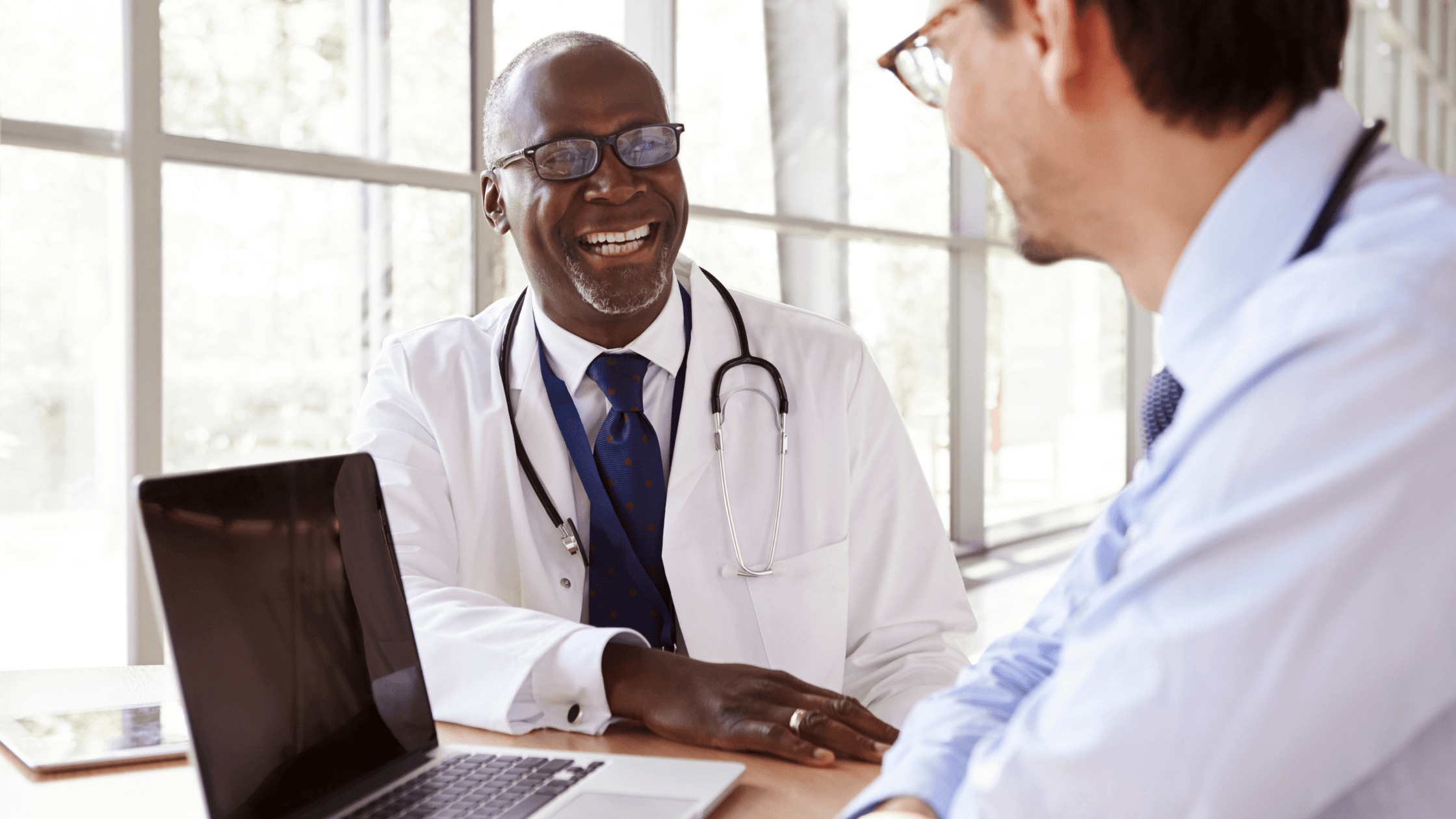 Orthodontist smiling and speaking to colleague using laptop